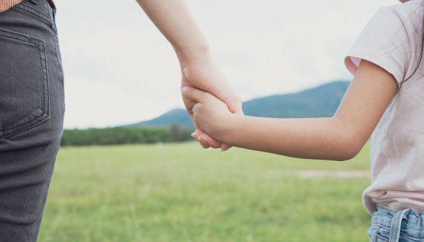 母亲牵着女儿的手走在绿油油的草地上。爱与保健概念图片下载