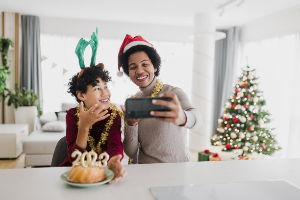 这对母子庆祝尼年，他们进行视频通话，吃带有金色蜡烛的2023数字圣诞蛋糕图片下载