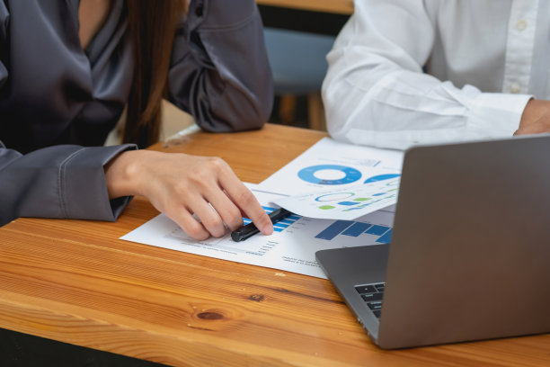 两名男性和女性营销人员使用公司文件和笔记本电脑记录数据，分析公司利润。图片下载