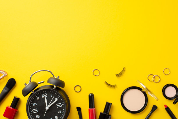 “黑色星期五”的概念。顶视图照片闹钟装饰化妆品紧凑型粉末指甲油假睫毛眼影唇彩刷子和金戒指上孤立的黄色背景与copyspace图片下载
