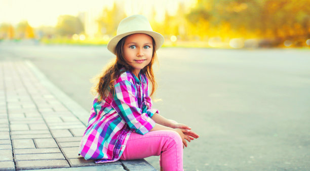 小女孩戴着夏天的草帽，穿着粉红色的格子衬衫走在城市的大街上图片下载