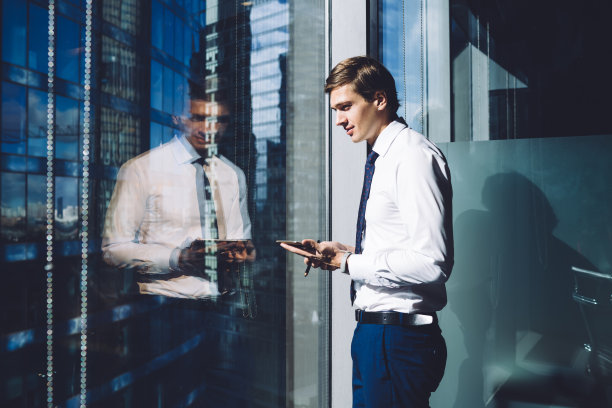 自信的商人用智能手机向窗外望去图片下载