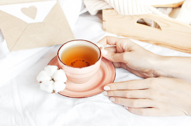 穿着白色针织衫的女子手捧一杯热茶，茶碟上放着精致的棉花。舒适的早餐在家里。生活方式温和背景复制空间秋冬概念图片下载