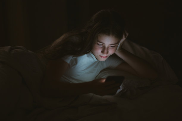 少年女孩晚上或晚上躺在床上看手机。手机成瘾。图片下载