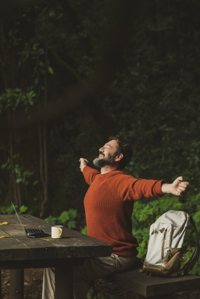 一名旅行男子下班后在自然森林里用笔记本电脑和漫游互联网连接展开双臂。人的概念与数字生活工作。快乐的成年男性背着背包。绿色图片下载