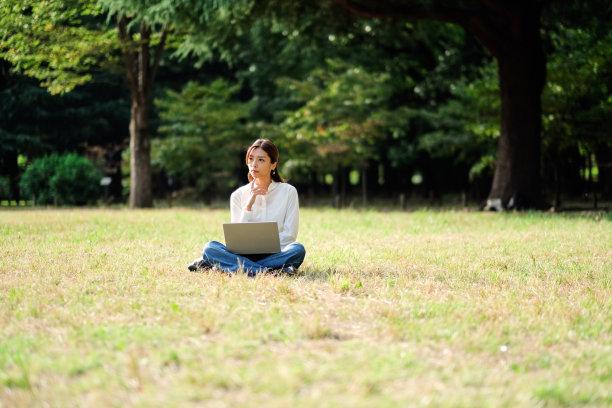 年轻女子坐在草坪上，在公园工作图片下载