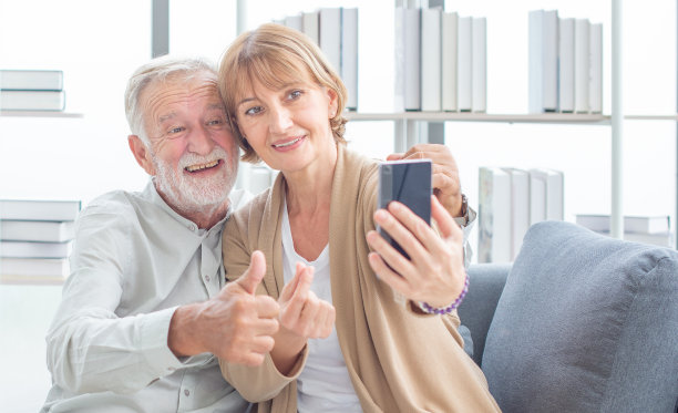 老夫妇一边用智能手机自拍，一边玩得很开心。幸福。退休。快乐有趣的成熟的老夫妇看着智能手机自拍图片下载