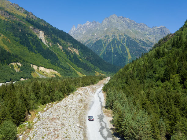 在一个阳光明媚的日子里，无人机拍摄的一辆汽车行驶在巨大的绿色山脉之间的峡谷中。旅游的概念，旅游图片下载