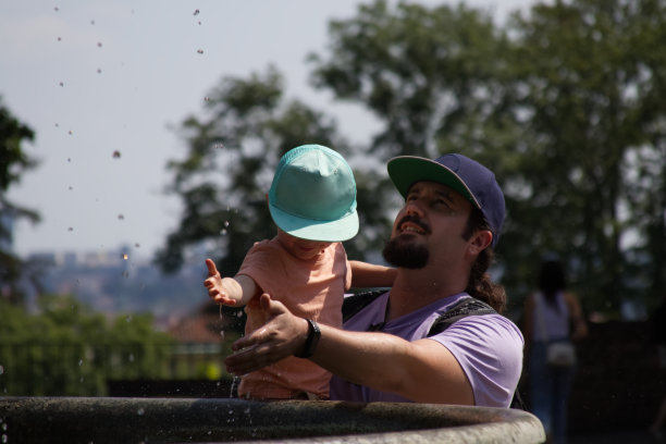 爸爸把儿子抱在怀里，他们用手接住喷泉的水滴图片下载