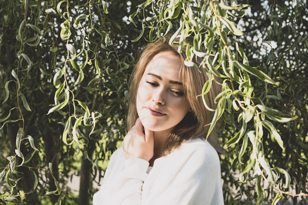 可爱的女人微笑在阳光下的柳树与树枝的影子。阳光明媚的日子里林地里的女性画像。图片下载