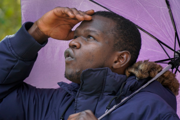 一个拿着伞的黑人男子的肖像，向上看并做手势图片下载