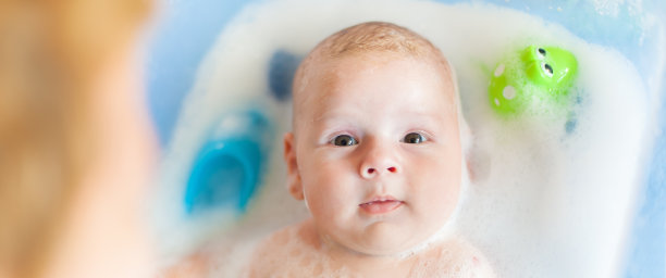 母亲在浴缸里给婴儿洗澡，浴缸里有水，肥皂泡冒出来图片下载