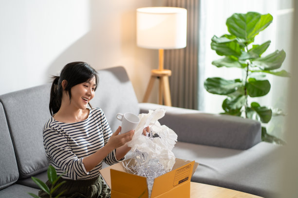 亚洲妇女开心地微笑着从网上购物打开纸盒，打开包装，检查产品。图片下载