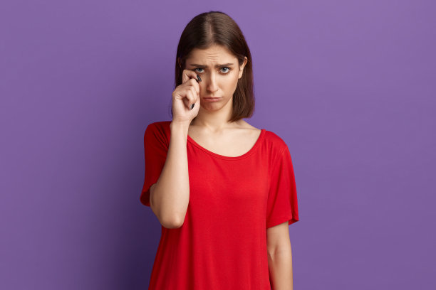 我有个问题。不满沮丧的年轻漂亮褐发女孩在红色t恤皱眉她的脸和摩擦她的眼睛，就像她在哭，是不满和不快乐。在紫色的墙上摆姿势。图片下载