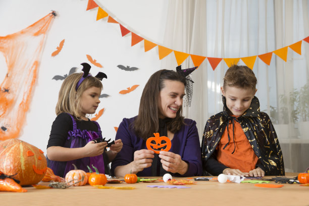 妈妈和两个孩子穿着化装舞会的服装为万圣节做装饰和工艺品图片下载