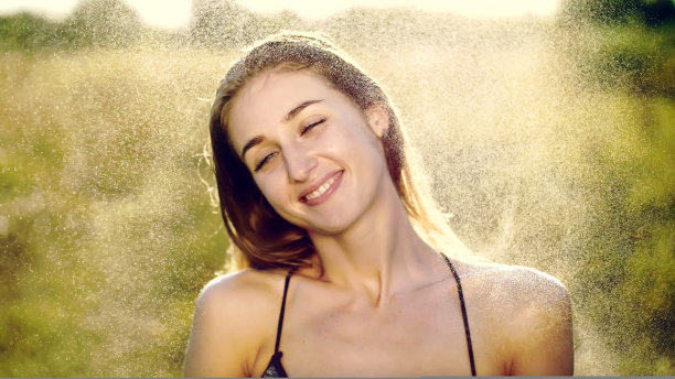 一个美丽的年轻金发女孩的肖像，在小夏雨下，在阳光下，在绿色的草地上。女孩微笑着，抚摸着她细腻美丽的白皙肌肤。高质量的照片图片下载