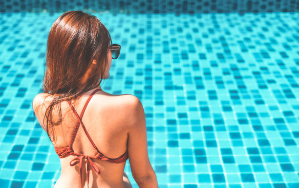 夏季时尚的女性。快乐性感微笑的女孩与健康的身体。比基尼里的健康皮肤。太阳的帽子。太阳镜，在旅游假期，在游泳池晒日光浴。美。健康。生活方式图片下载