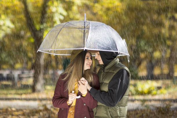 秋天的公园里，一对年轻夫妇在一把透明的伞下拥抱图片下载