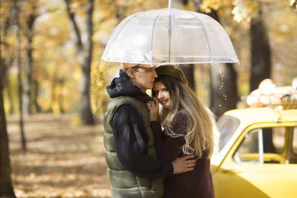 秋天的公园里，一对年轻夫妇在一把透明的伞下拥抱图片下载
