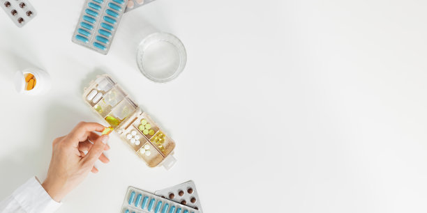 药盒每日服药，有片剂和胶囊。妇女拿着药片，药物治疗和健康。桌子、横幅、复制空间上的药药盒和一杯水图片下载