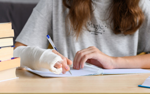 一个手受伤(手指骨折)的女孩试图在笔记本上写字。一个胳膊上缠着膏药的女孩正试着做家庭作业。特写，选择性窄聚焦。图片下载