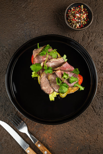 烤鸡胸肉，肉片和新鲜蔬菜，黑色的碗，深色的背景。图片下载