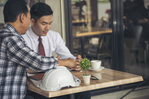 亚洲工程师头脑风暴建筑承包商土木工人伙伴团队会议在施工现场。图纸工程师，安全帽工人，头盔放在桌子上。工程师团队合作咨询图片下载
