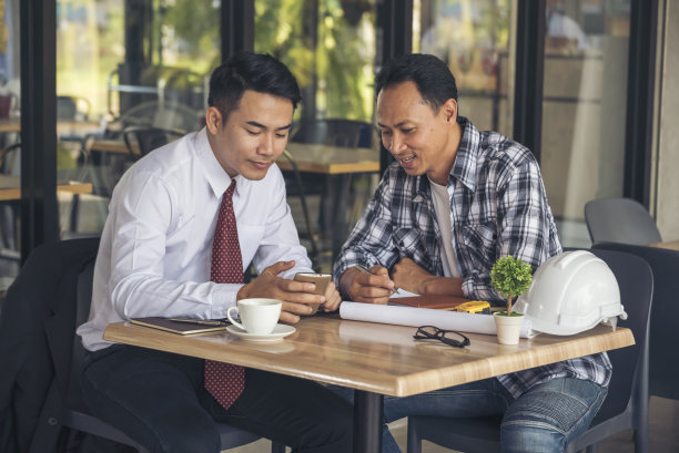 亚洲工程师头脑风暴建筑承包商土木工人伙伴团队会议在施工现场。图纸工程师，安全帽工人，头盔放在桌子上。工程师团队合作咨询图片下载