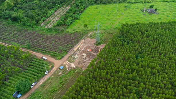 高空鸟瞰图挖掘机正在高压塔架的基础和高压杆子的腿上工作。森林中电线建设的俯视图。图片下载