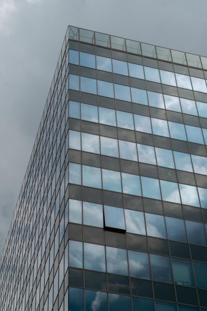 在匈牙利布达佩斯的灰色天空下，一座高大的现代建筑的玻璃窗户垂直拍摄图片下载