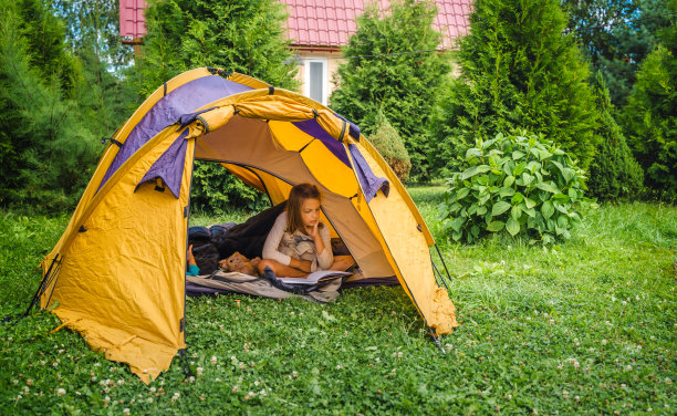 小孩子，小孩子在橙色的旅游帐篷里玩耍，看书。家庭旅行，远足大自然。后院游戏，玩得很开心。户外休闲活动。自组装，在草坪、草地上搭建露营帐篷图片下载