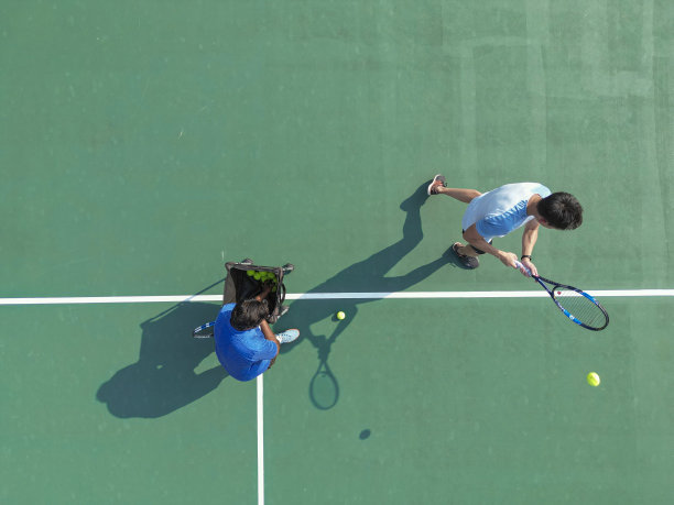 无人机视角的运动训练亚洲中国网球运动员在教练指导下，直接在网球场练习发球图片下载