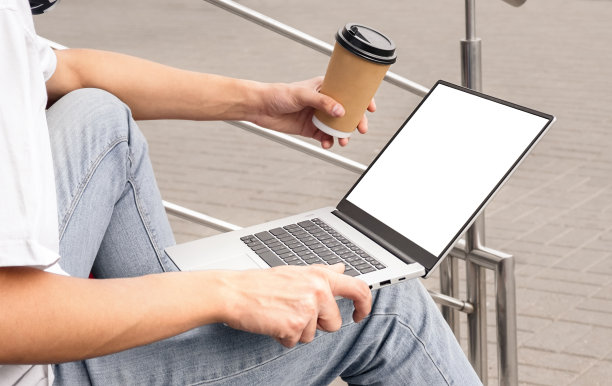 笔记本电脑白色屏幕和咖啡杯在男性手中。复制空间，选择性聚焦图片下载