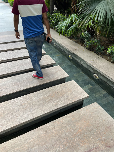 特写图像，无法识别的人走过矩形的踏石，穿过正式的，瓷砖花园池塘，铺就的路径，花坛灌木，水反射，关注前景图片下载