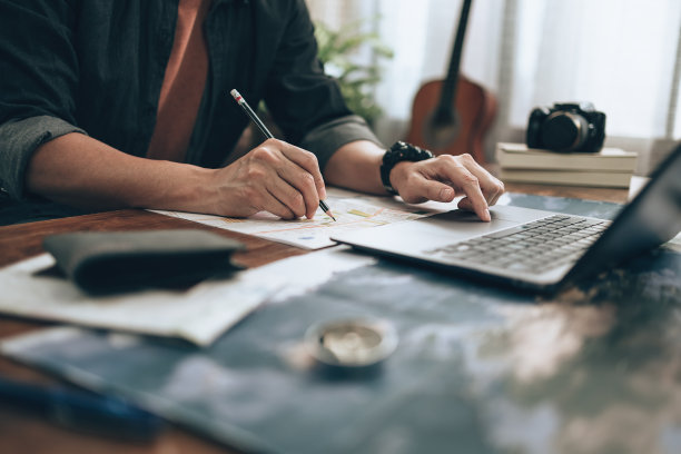 旅行者计划用铅笔在地图上做标记，用笔记本电脑在地图上做标记，或查找旅行路线。旅行的概念。图片下载