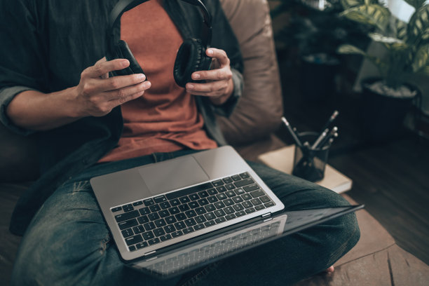 男人们拿着耳机，坐在家里的沙发上听音乐，检查音乐创作者的旋律。放松的家的概念。图片下载