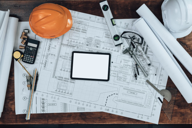 在办公桌上进行图纸检查，在图纸上进行计算器，三角尺，安全眼镜，指南针，游标卡尺等工程工作。工程师，建筑师，工业和工厂概念。图片下载