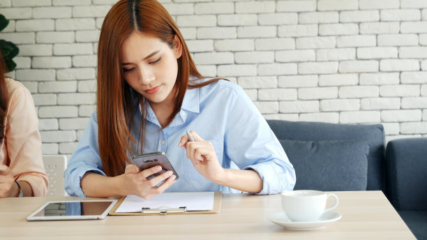 亚洲女性通过智能手机聊天，在家里的小办公桌上工作。年轻的亚洲女性手握手机科技生活方式。快乐女性的人打电话使用数字智能电话工作在家庭办公室图片下载
