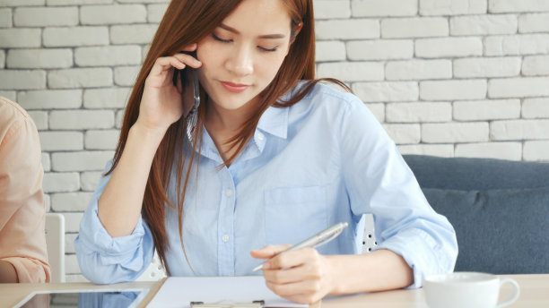 亚洲女性通过智能手机聊天，在家里的小办公桌上工作。年轻的亚洲女性手握手机科技生活方式。快乐女性的人打电话使用数字智能电话工作在家庭办公室图片下载