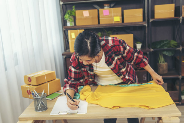服装设计师妇女在桌子上测量服装设计包装盒。妇女检查货物的大小，质量到送货箱包装。企业家亚洲女性在家里的办公桌上开始小生意图片下载