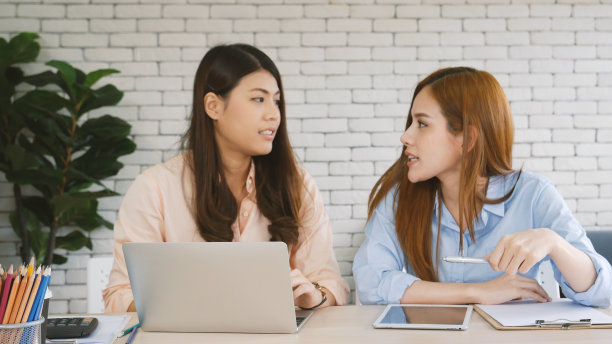 两个女商人在公司办公桌旁用笔记本电脑开会。两个年轻的女性自由职业阅读金融图表策划分析市场数据。亚洲人团队工作办公室公司。图片下载