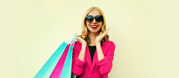 美丽的快乐微笑的年轻女子与彩色购物袋穿着粉红色的商务运动夹克的背景图片下载
