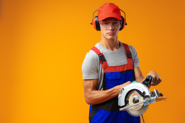 年轻的男性建筑工人与现代圆锯在黄色的工作室背景图片下载