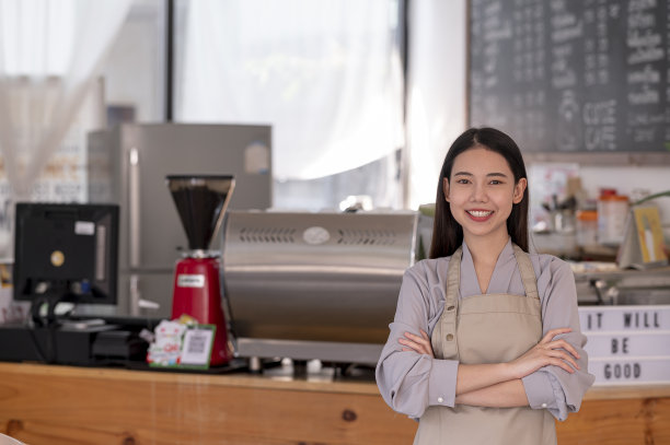 咖啡生意的老板，有吸引力的年轻美丽的白人咖啡师在围裙与交叉的手微笑的相机在咖啡店柜台。图片下载