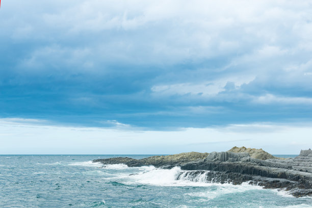 由柱状玄武岩在暴风雨的大海背景下形成的岩石海岸，千岛群岛的海岸景观图片下载