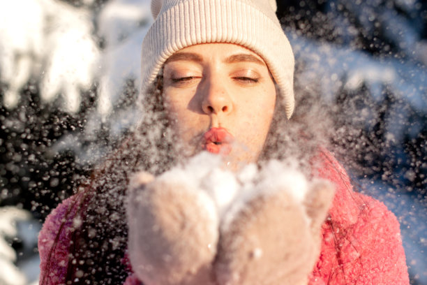 年轻漂亮的女人正在吹掉手上的雪。冬天，圣诞节和新年快乐的概念。图片下载