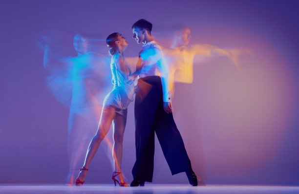 美丽的女人和苗条的男人，一对交际舞舞者在舞台服装跳舞孤立的紫色背景在霓虹灯混合光。图片下载