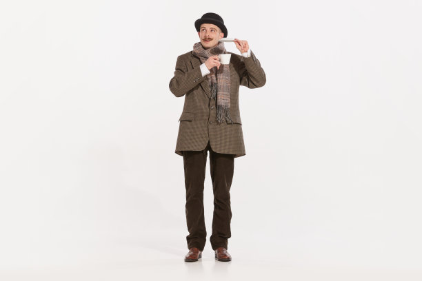 肖像的时尚男子在西装，大衣和帽子摆姿势与茶杯在白色背景。英国人图片下载