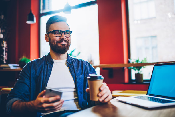 愉快的男性远程工作人员穿着休闲装得到好消息，同时与设备在咖啡馆工作图片下载