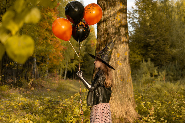 有趣的小女孩穿着万圣节的女巫服装，带着黑色和橙色的气球。图片下载